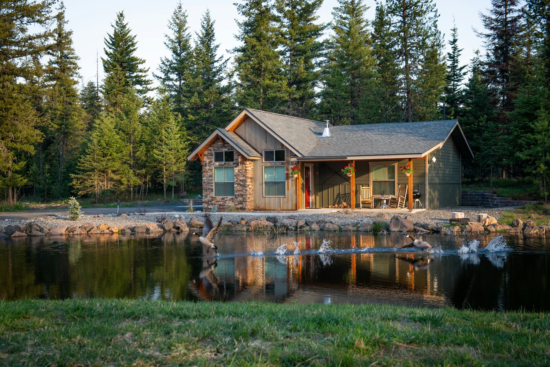 Cabin beside a reflective pond and evergreen forest